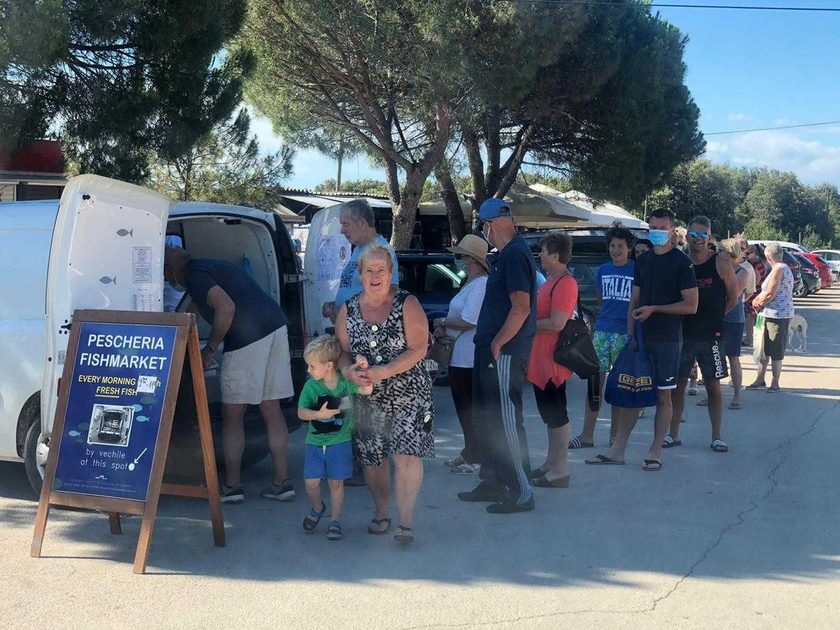 Queue of summer customers beside a white delivery van and a navy Pescheria Fishmarket A-frame sign