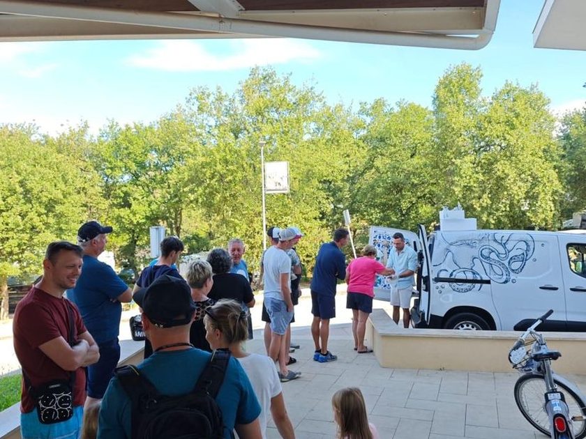 Customers gathered at the open rear doors of a white van with an octopus line drawing on the side, under a wooden pergola